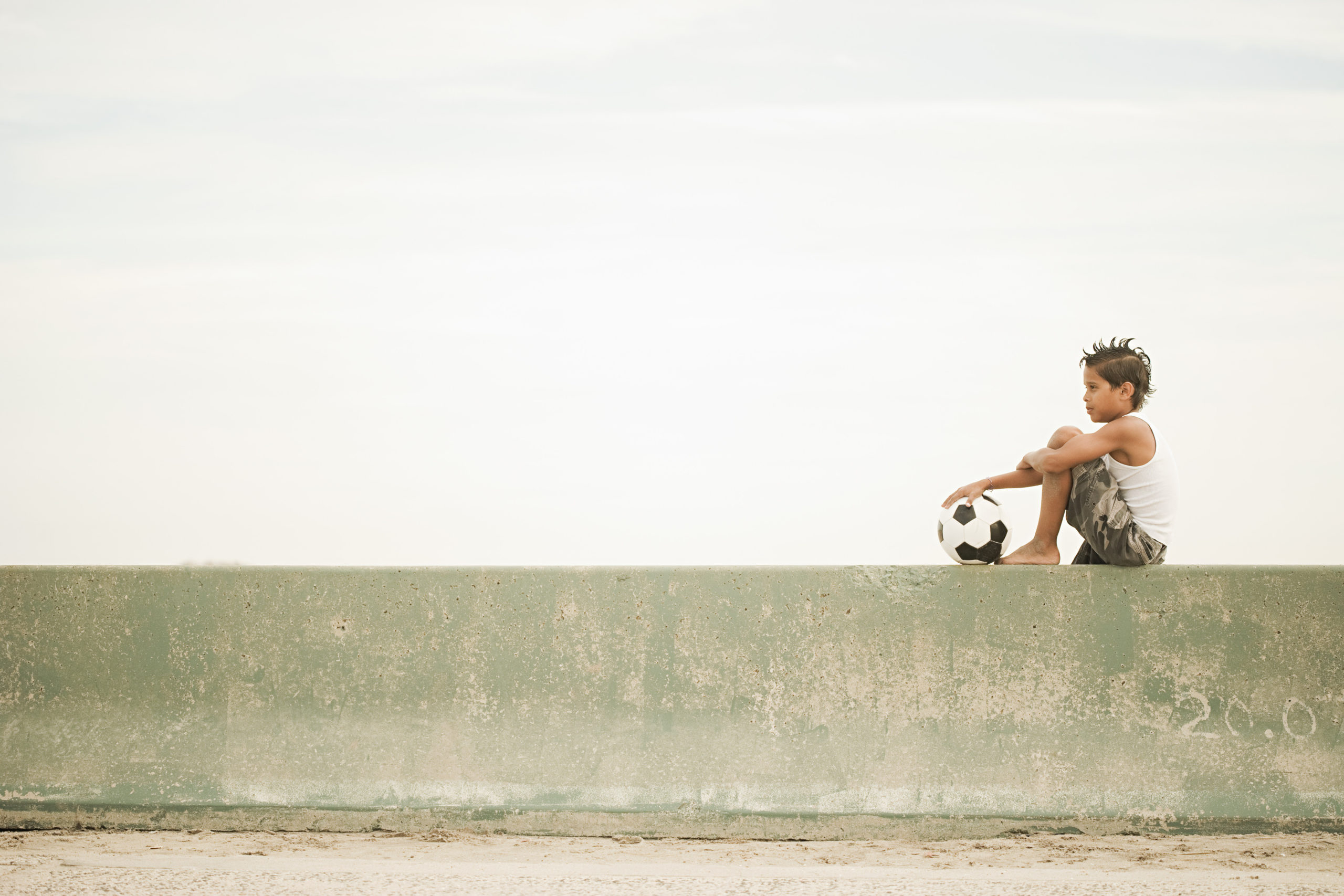 Boy sitting on wall with football